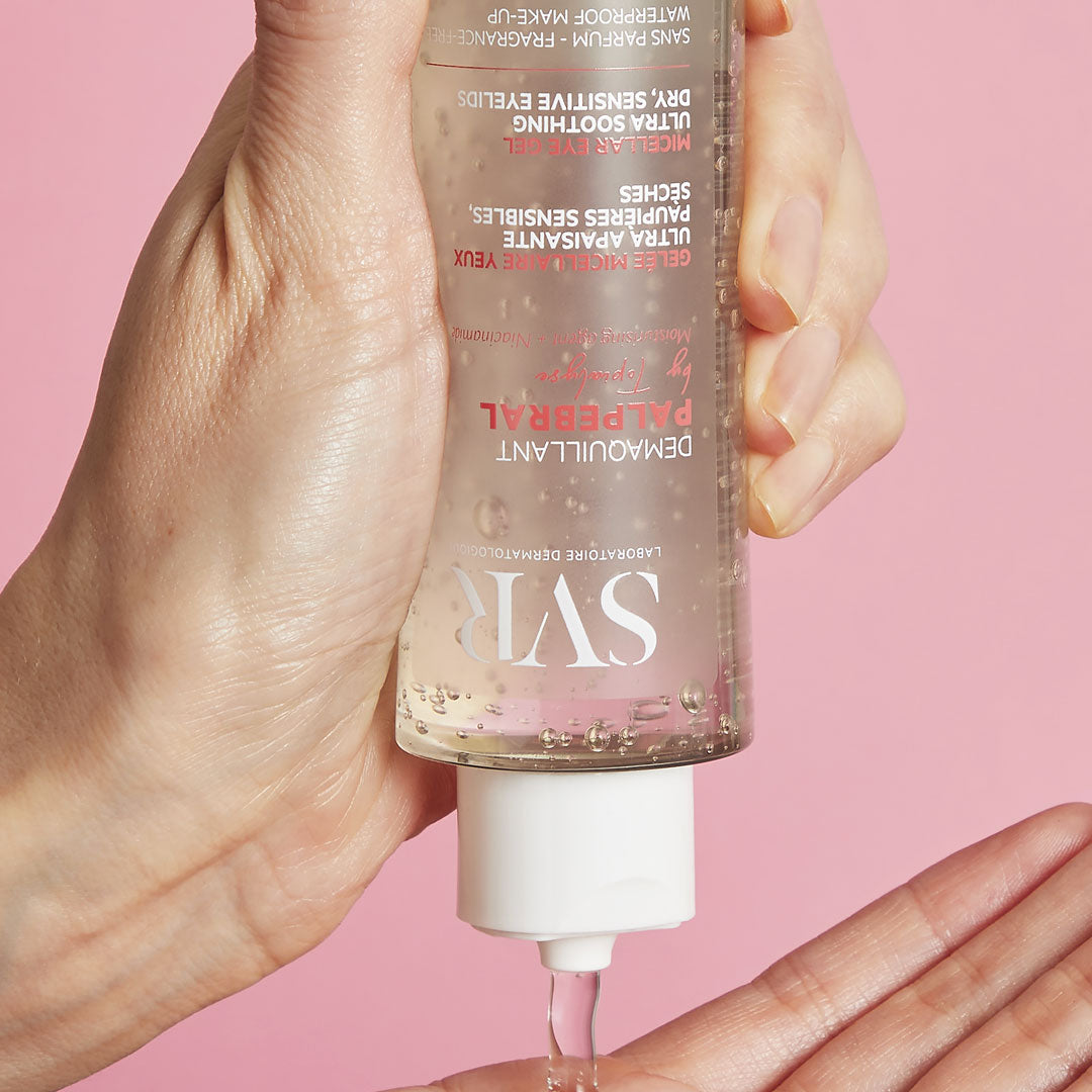 Frasco transparente de gel desmaquilhante SVR Palpebral a ser aplicado na palma da mão sobre fundo rosa.