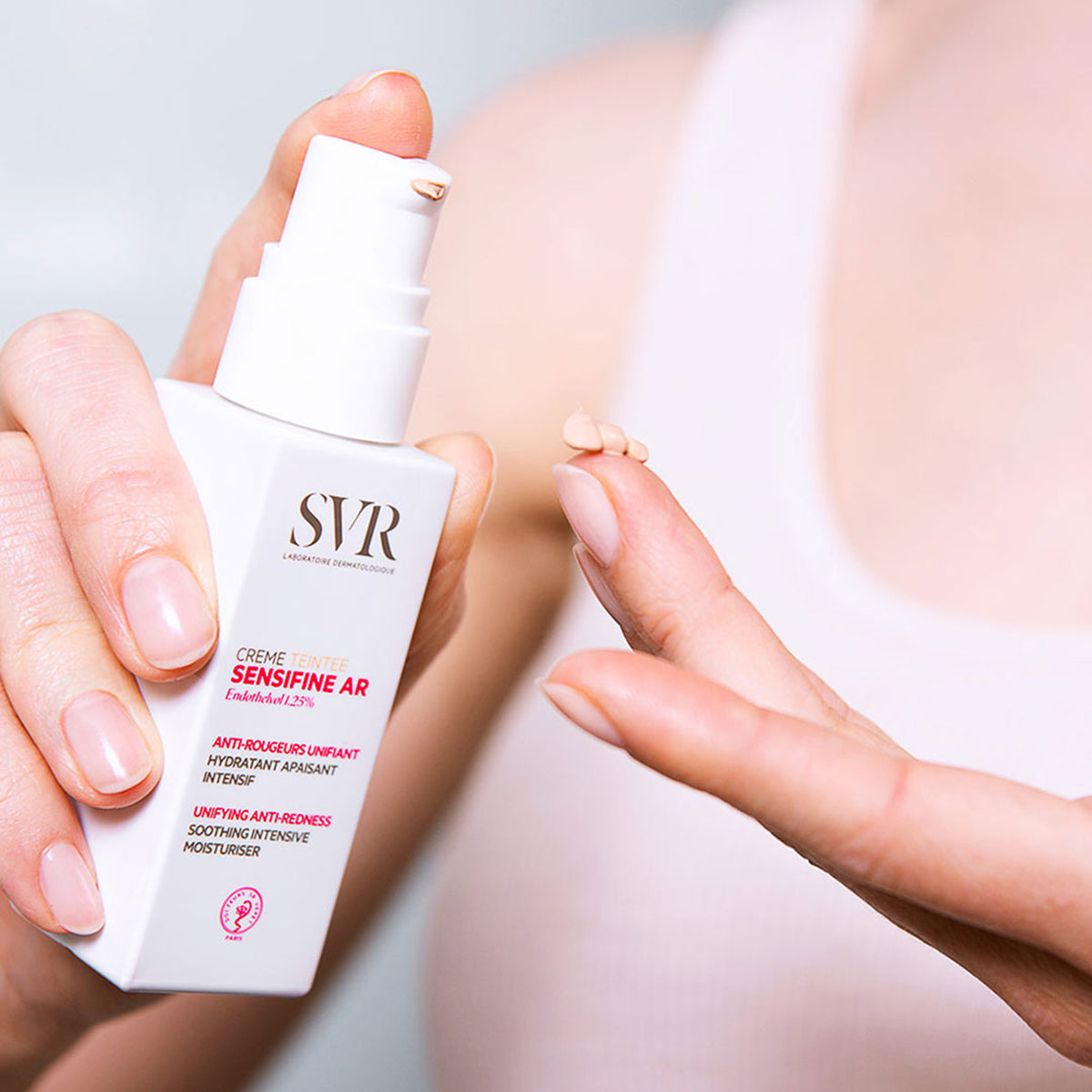 Frasco branco de SVR Sensifine AR Creme Teintée com doseador, mostrando a textura bege do creme na ponta do dedo.