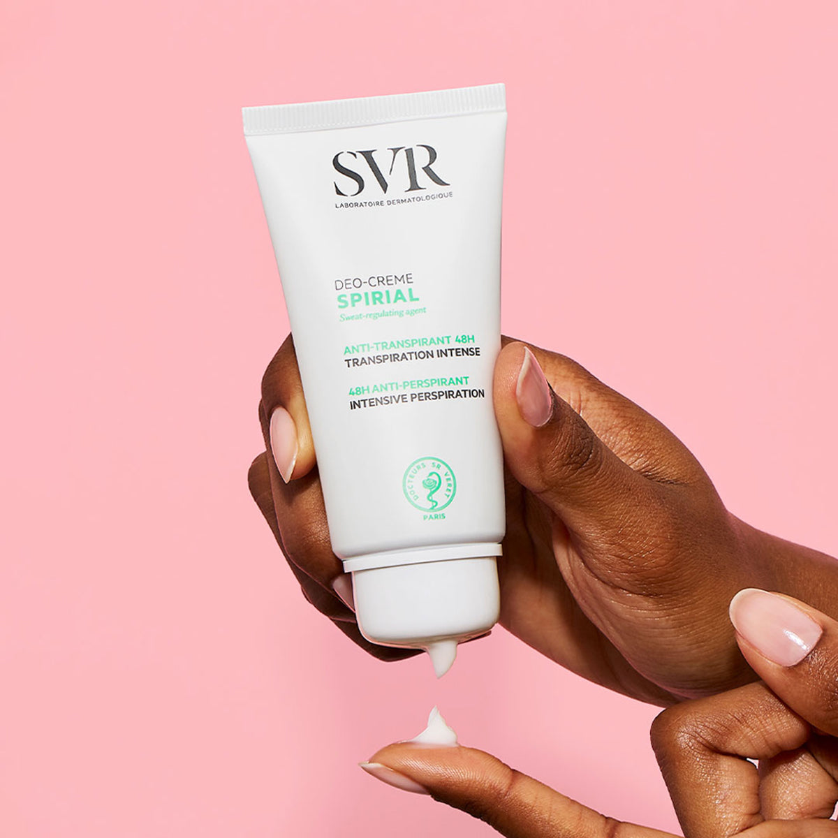Tubo branco de creme antitranspirante SVR Spirial sendo aplicado na mão sobre um fundo rosa suave.