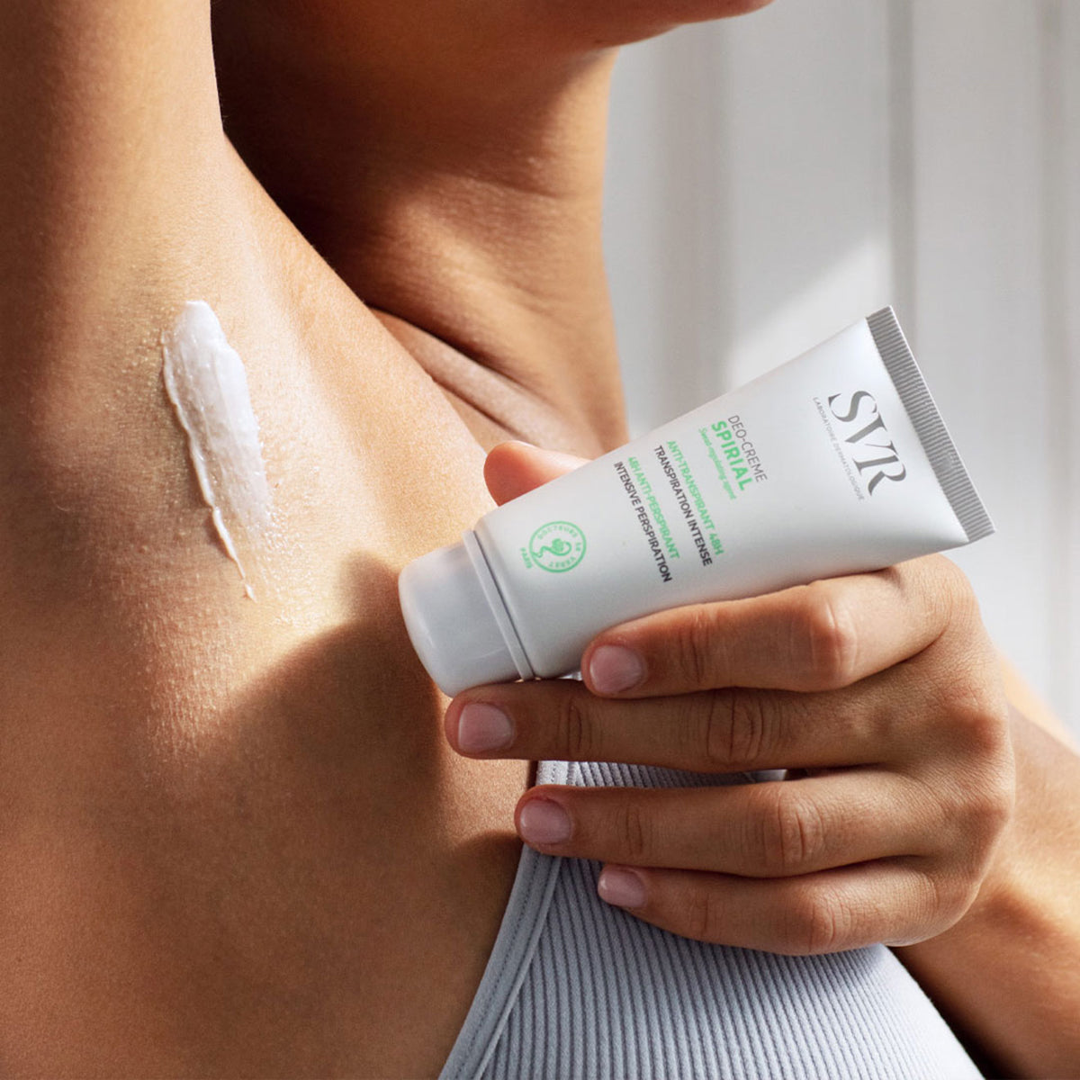 Tubo branco de creme antitranspirante SVR Spirial sendo aplicado na axila com textura suave e acabamento invisível.