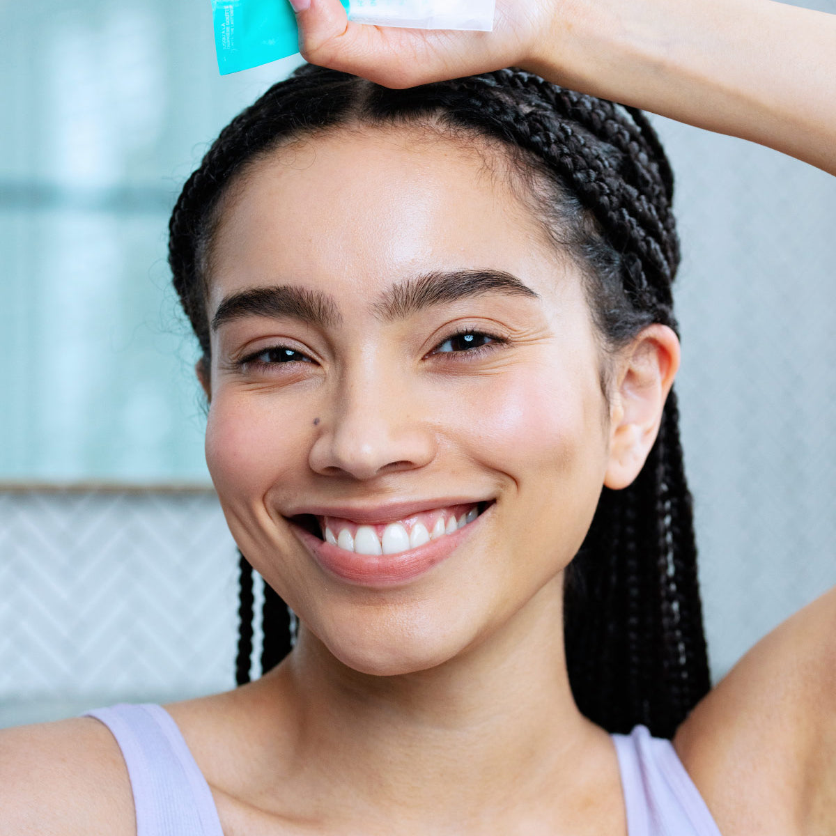 Mulher sorridente com tranças segurando a bisnaga azul e branca do creme hidratante Hydraliane Creme Riche.