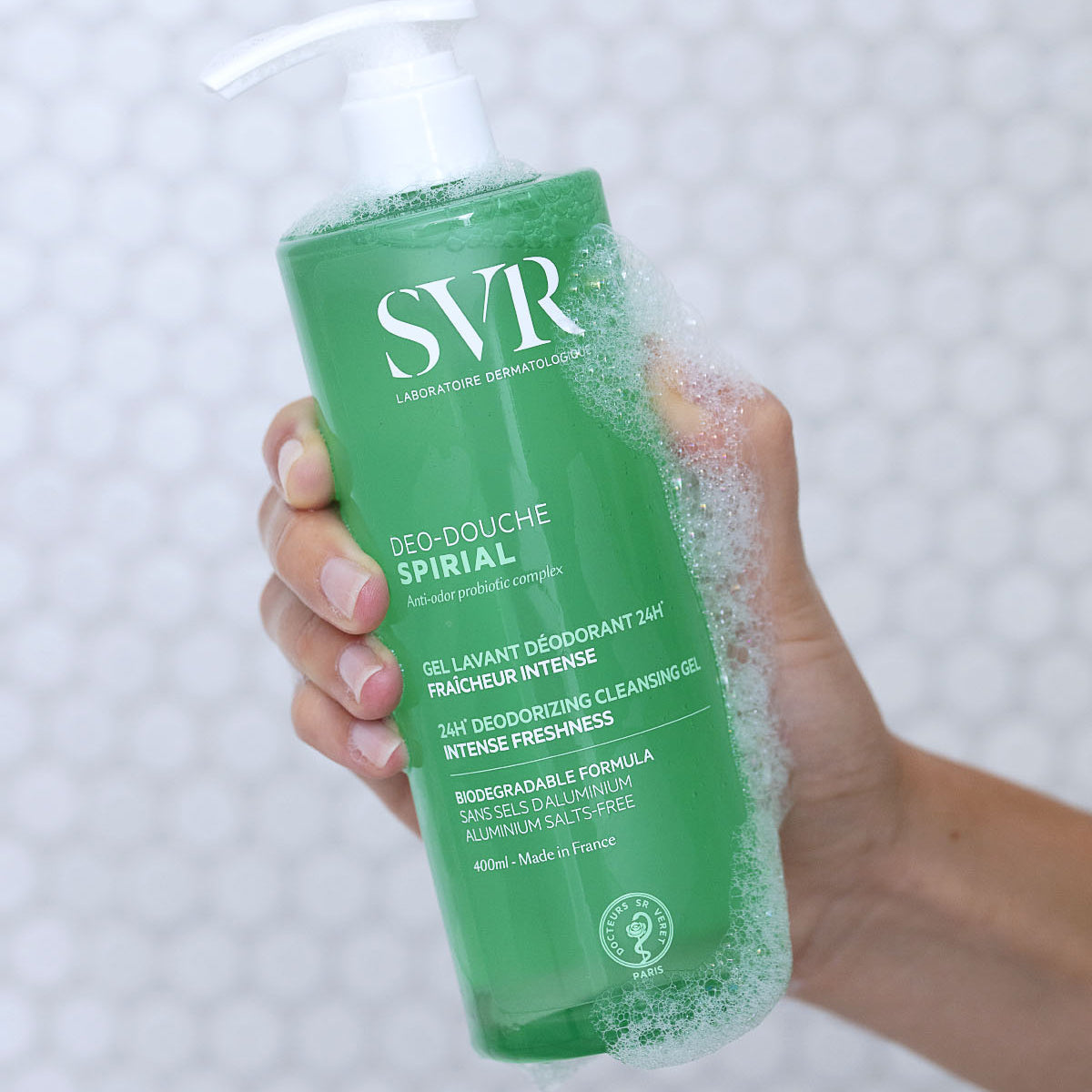 Frasco verde de 400ml do gel de duche SVR Spirial Deo-Douche com doseador, segurado por uma mão com espuma.