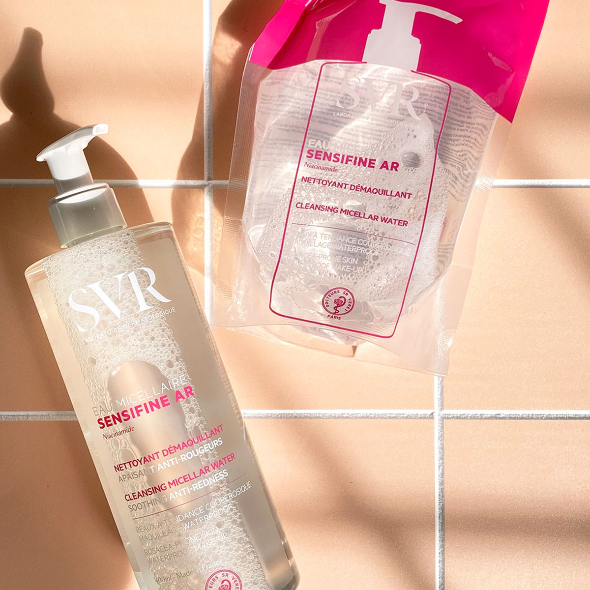 Frasco de 400ml e recarga de SVR Sensifine AR Eau Micellaire sobre azulejos bege, com design transparente e bomba doseadora.