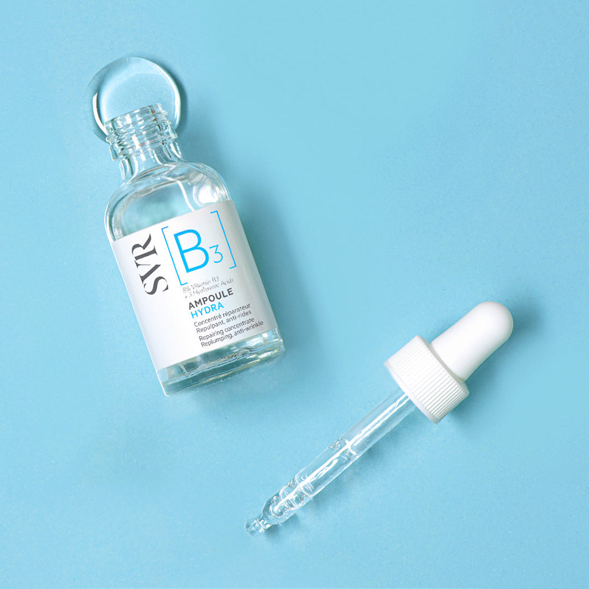 Frasco de vidro transparente SVR Ampoule Hydra com conta-gotas aberto sobre fundo azul claro.