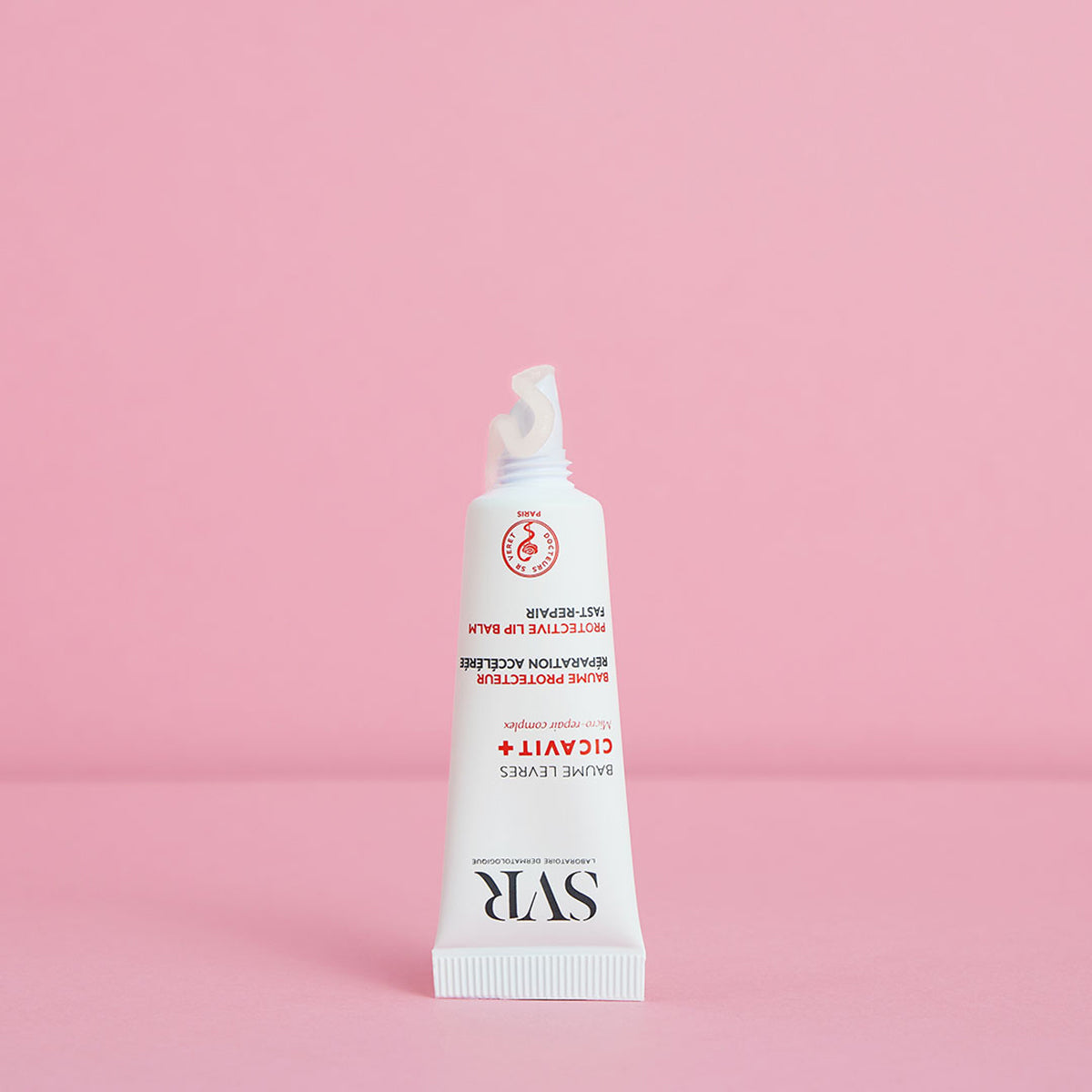 Tubo branco de bálsamo labial reparador SVR Cicavit+ Lèvres com textura transparente sobre fundo rosa.