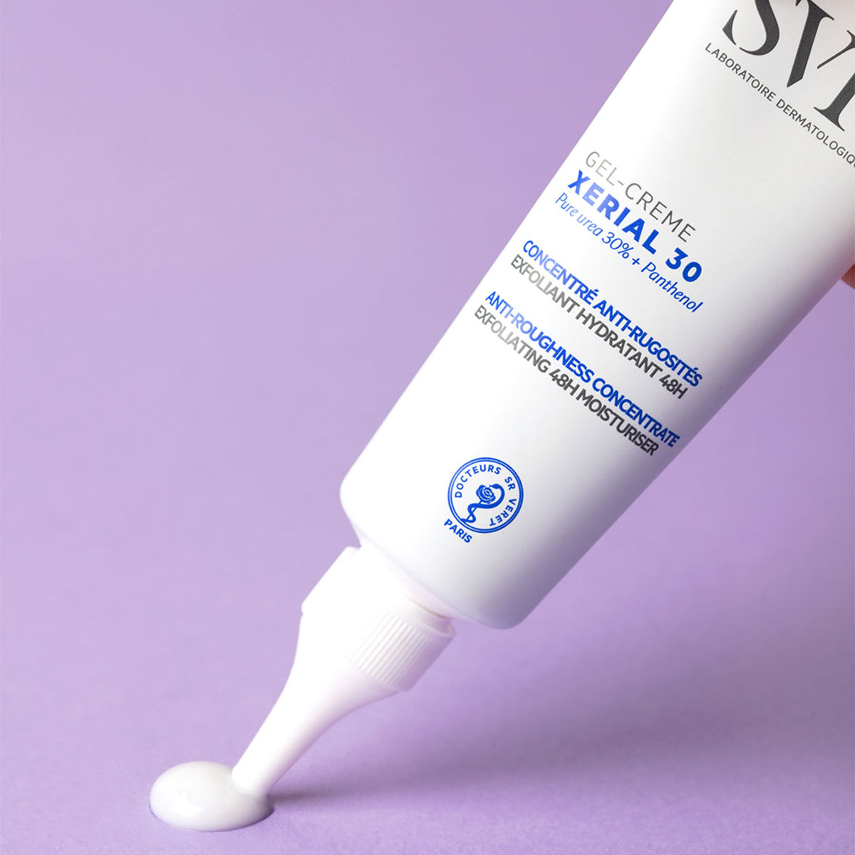 Tubo branco de SVR Xerial 30 Gel-Crème dispensando uma gota de creme sobre fundo lilás suave.