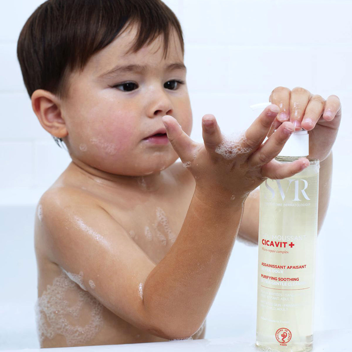 Criança a usar o gel de limpeza SVR Cicavit+ com doseador numa embalagem transparente, criando espuma suave nas mãos.