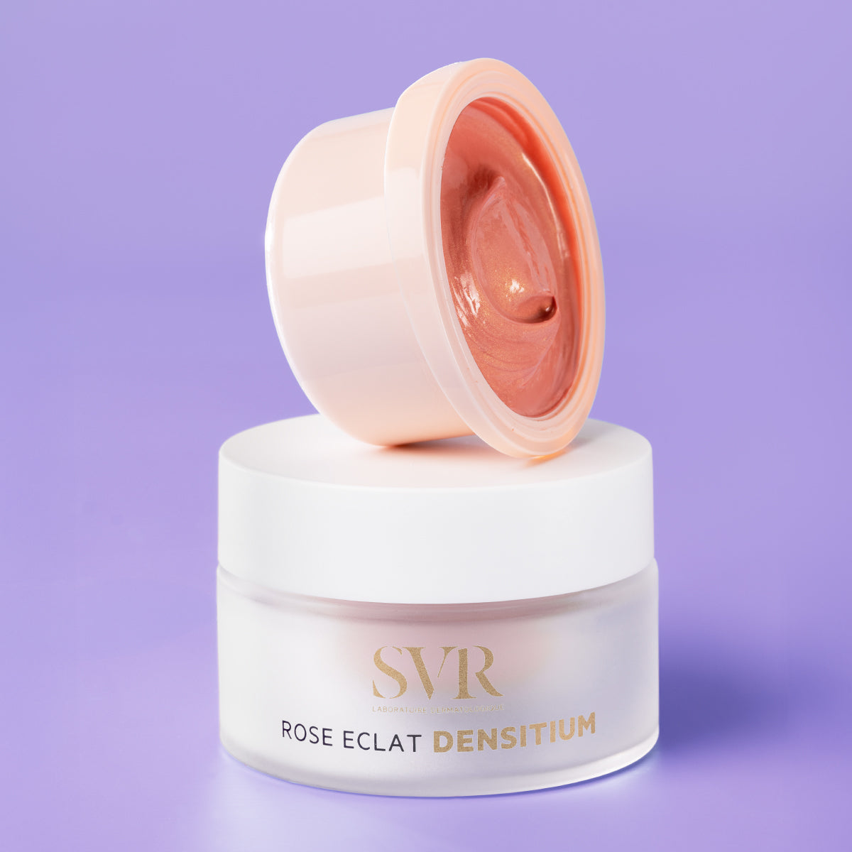 Creme facial SVR Densitium Rose Eclat em frasco de vidro fosco com tampa branca e textura rosada iluminadora sobre fundo lilás.
