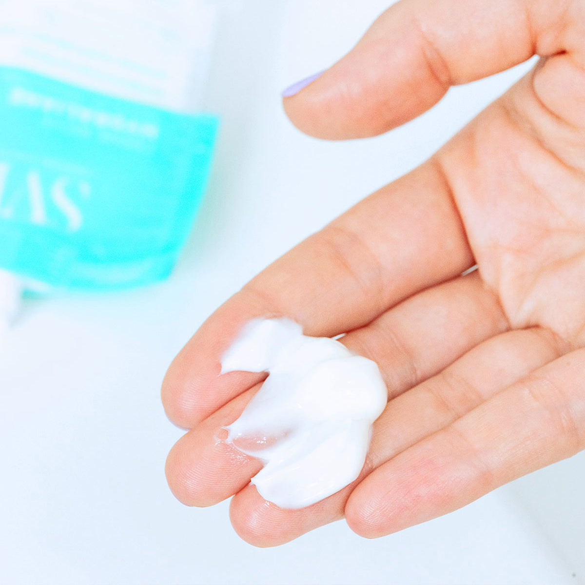 Creme hidratante branco e rico na palma da mão, com embalagem azul Hydraliane ao fundo.
