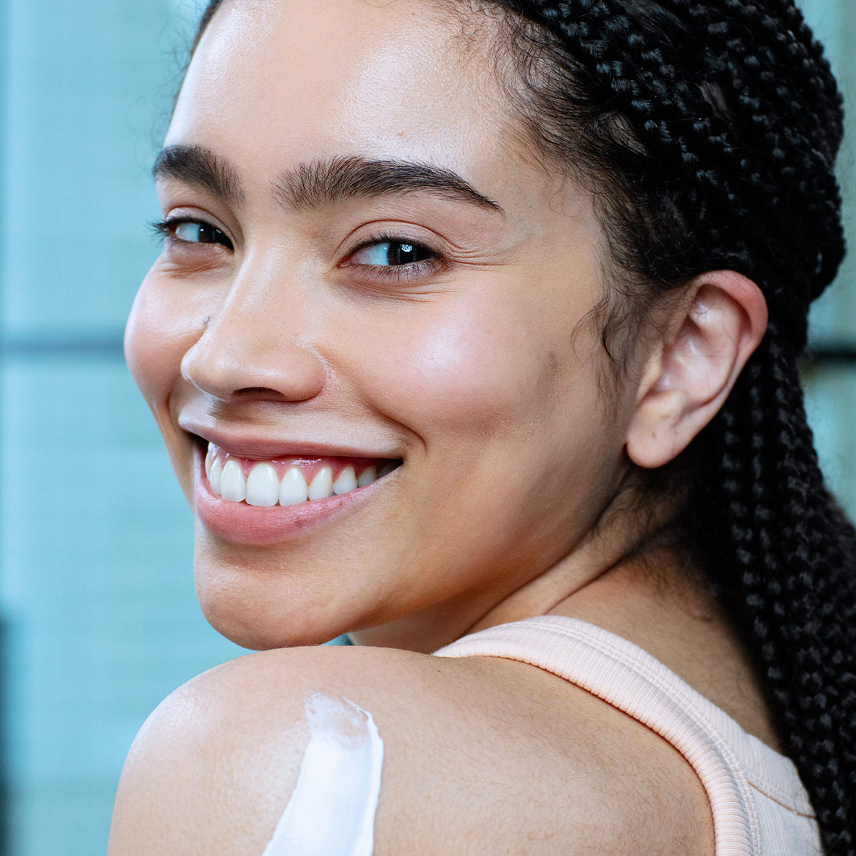 Mulher sorridente aplicando loção hidratante Xerial 10 Lait Corps na pele do ombro, com textura cremosa e acabamento suave.