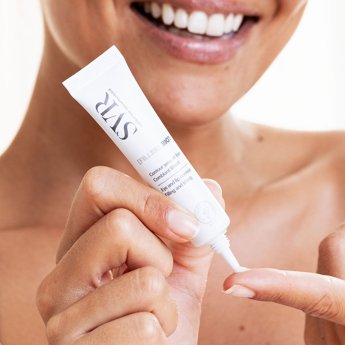 Tubo branco de creme SVR [FILLER] BIOTIC sendo aplicado no dedo por uma mulher sorridente.