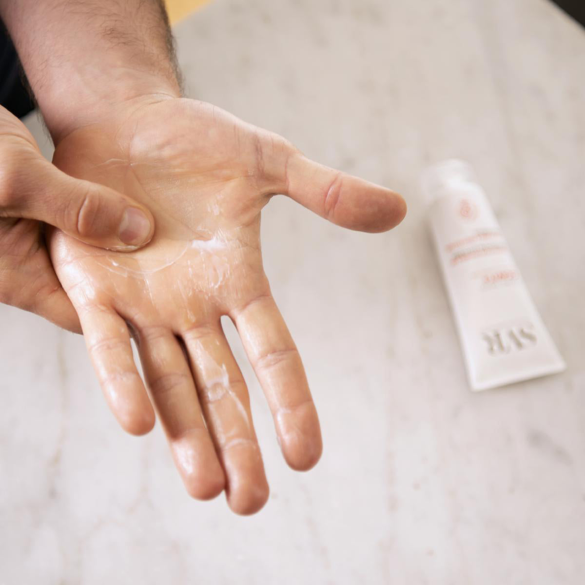 Creme reparador Cicavit+ aplicado na palma da mão, com bisnaga branca SVR ao fundo sobre superfície de mármore.