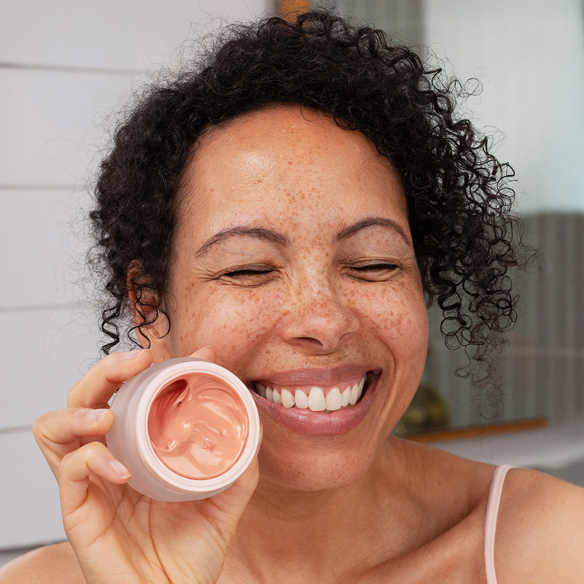 Mulher sorridente segura um frasco de creme facial DENSITIUM Rose Eclat com textura rosada e iluminadora.