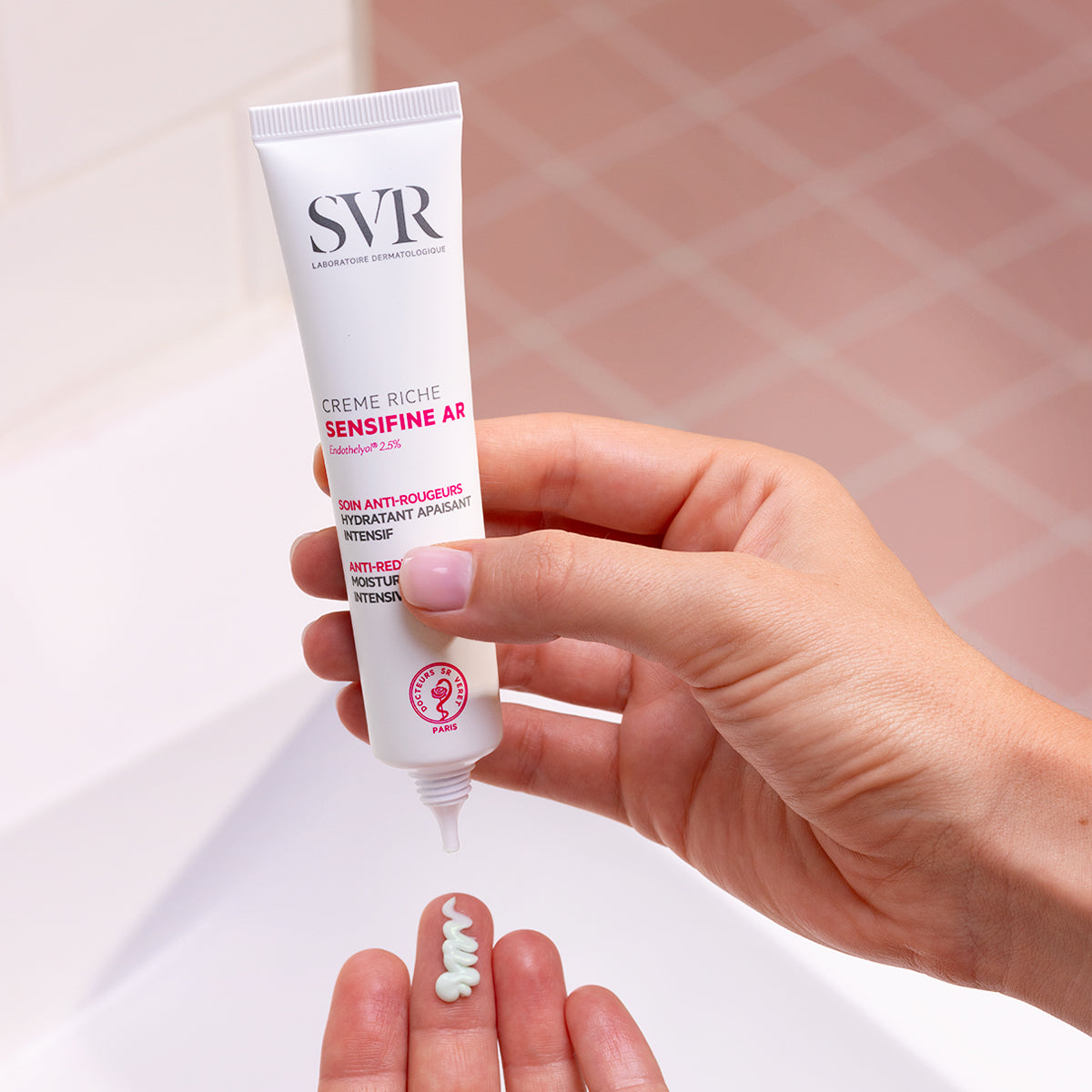 Hand squeezing white SVR Sensifine AR Creme Riche tube, dispensing a dollop of light green soothing face cream onto palm.