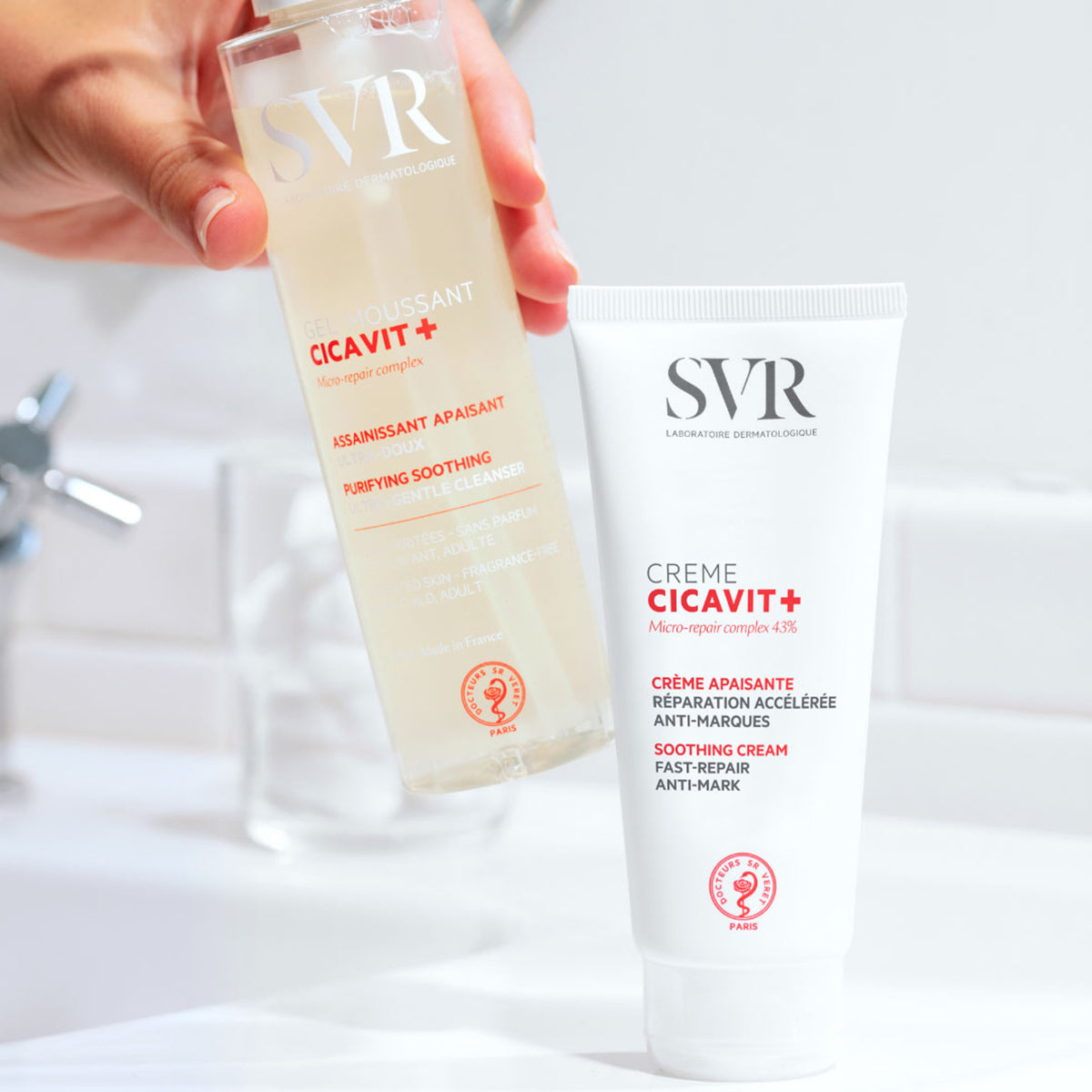 Frasco transparente de gel de limpeza SVR Cicavit+ ao lado de um tubo branco de creme reparador em ambiente de casa de banho.
