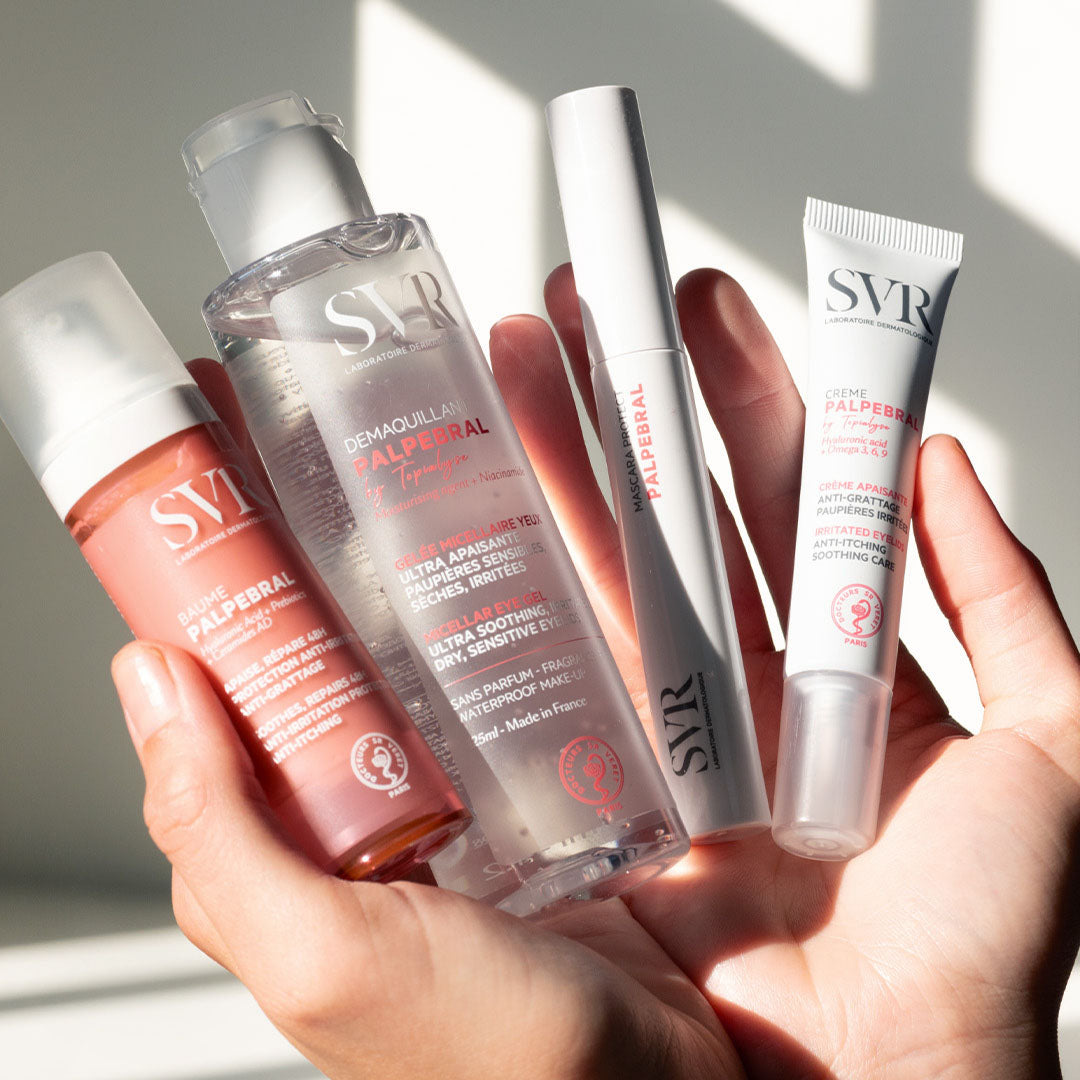 Mão segurando quatro produtos SVR Palpebral, incluindo gel desmaquilhante, bálsamo, máscara e creme para olhos em embalagens brancas.