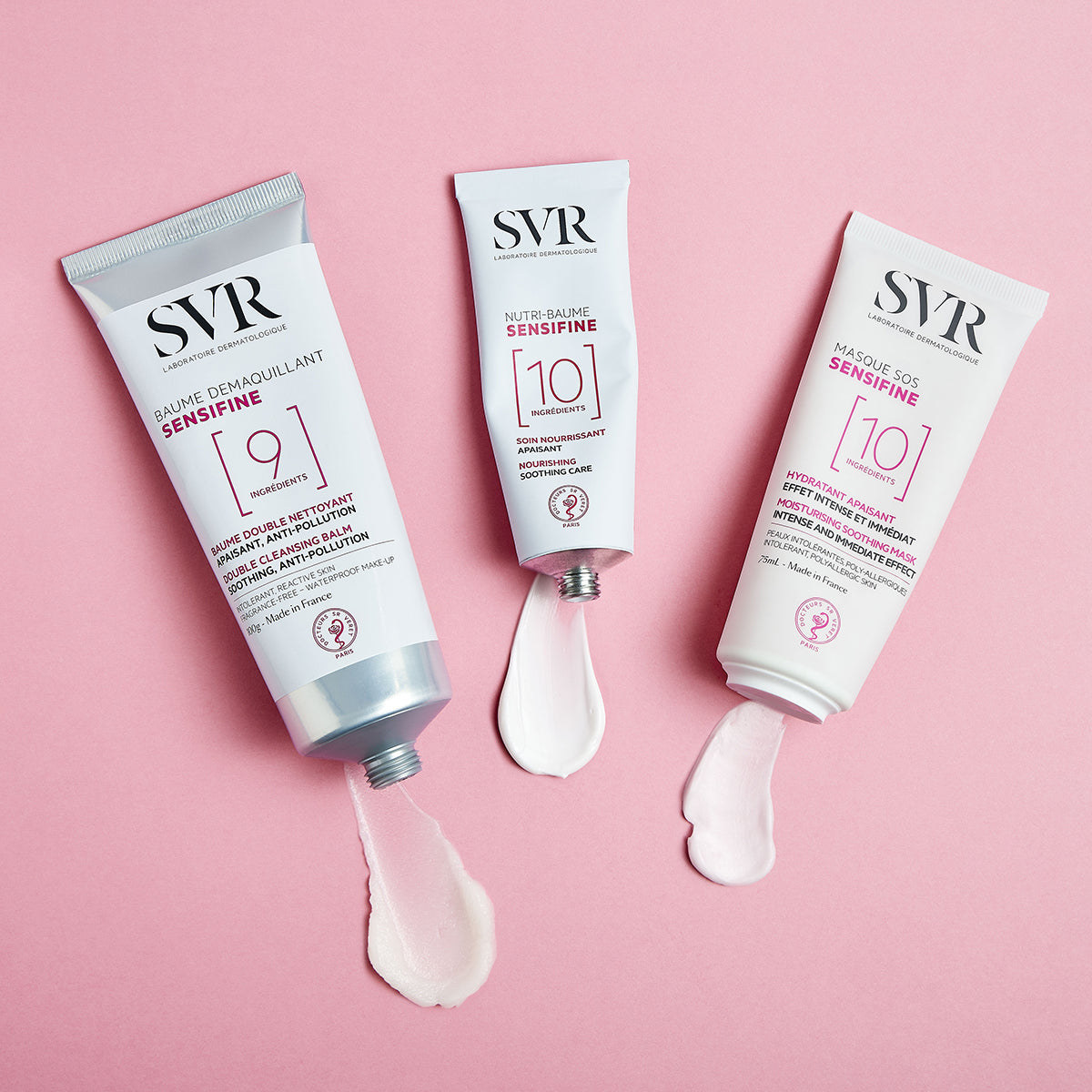 Três bisnagas de produtos SVR Sensifine com texturas em creme sobre fundo rosa, destacando o bálsamo e máscaras de limpeza.