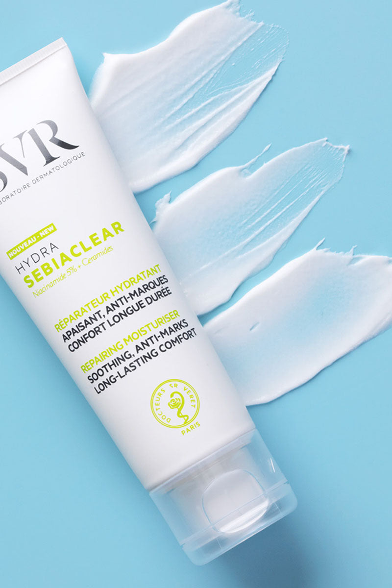 Tubo branco de hidratante SVR Sebiaclear Hydra com textura cremosa espalhada sobre fundo azul claro.