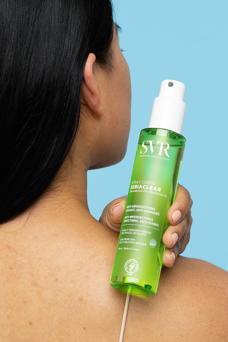 Frasco verde de spray corporal SVR Sebiaclear para pele com imperfeições sendo aplicado nas costas.