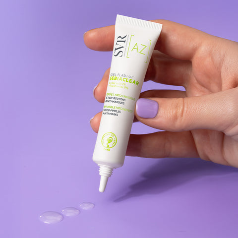 Hand holding a white SVR Sebiaclear Gel Flash 4H tube with clear gel drops on a purple background.
